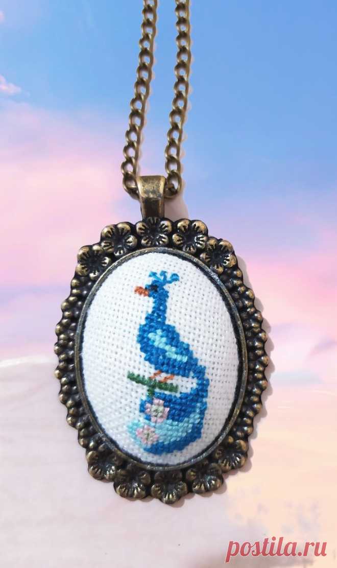 a cross - stitch necklace with a blue bird on it's side and a sky background