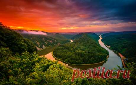 Saarschleife On the Saar river in Germany is the Saarschleife, where the river makes a spectacular hairpin turn. I got up early to watch the sunrise and it is amazing to see just how different nature presents itself every time. As the sun started to rise the clouds are lit up almost burning orange as mist gently lifts from the valley.