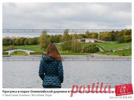 Прогулка в парке Олимпийской деревни в Москве ранней осенью. Девушка в голубой куртке около пруда на фоне зелёного парка и серого неба. (2016 год) Стоковое фото, фотограф Анастасия Усанина / Фотобанк Лори